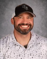 Smiling man in a black cap and white speckled shirt against a gray background