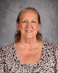 Portrait of a smiling woman in a patterned blouse against a gray backdrop