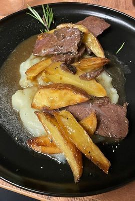 Un primo piano di un piatto di cibo con carne e patate su un tavolo.