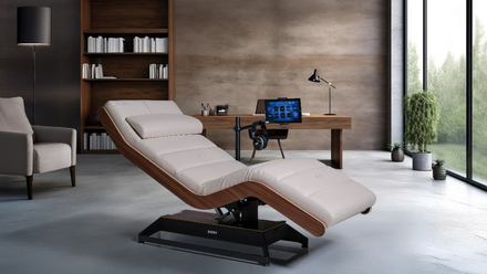 Modern massage table in a sleek office with desk, laptop, chair, and large windows