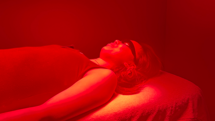 Person lying on a padded table under red light, head turned to the side.