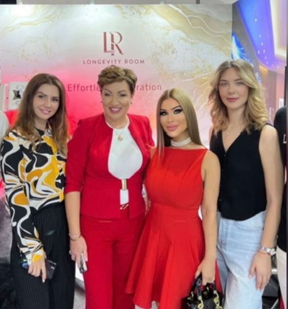 Four women posing indoors in front of a Longevity Room event backdrop, dressed in bright stylish outfits.