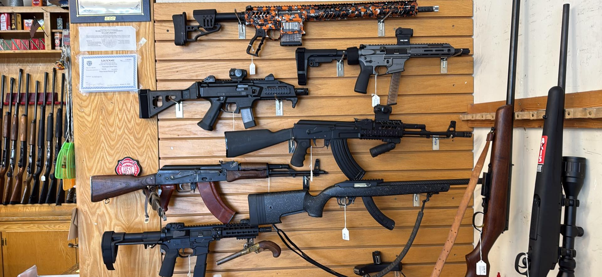 Guns displayed on wooden wall in gun store. Various firearms including rifles and pistols, with different colors and styles.