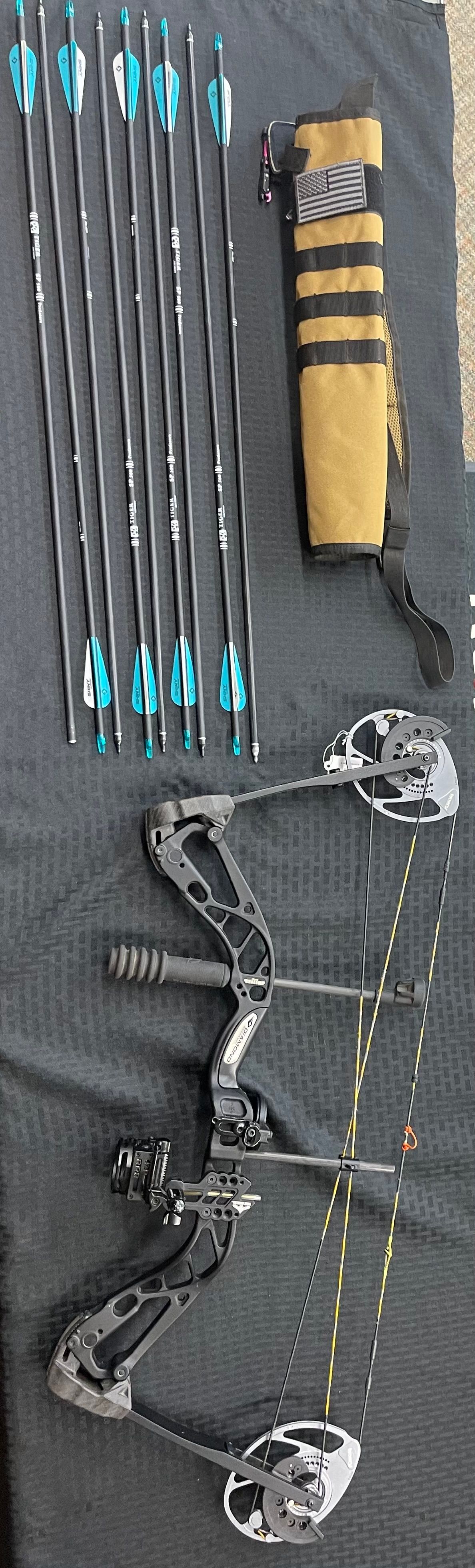 A camouflage compound bow, several arrows with blue fletching, and a matching quiver laid out on a gray surface.