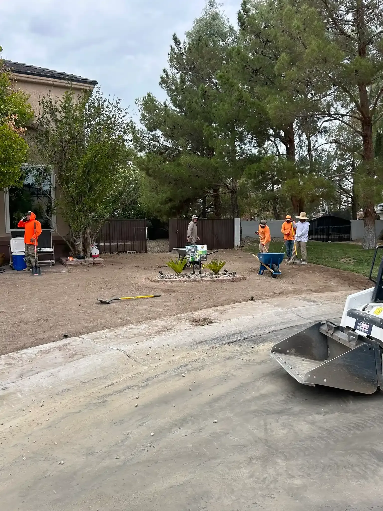 Workers loading a truck on a road beside an orange construction sign and palm trees.