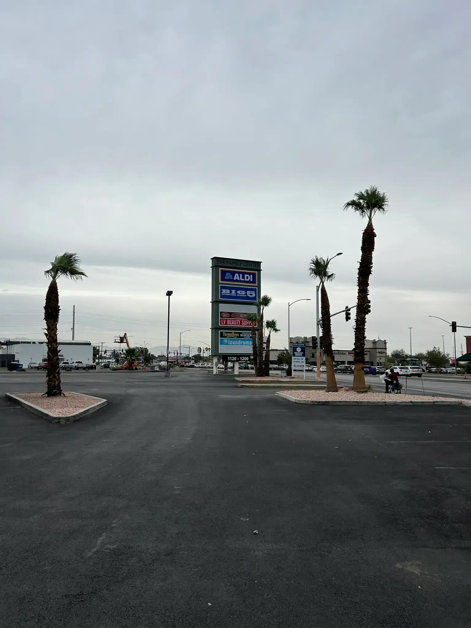 Palm-lined parking lot with a tall gas station sign under an overcast sky