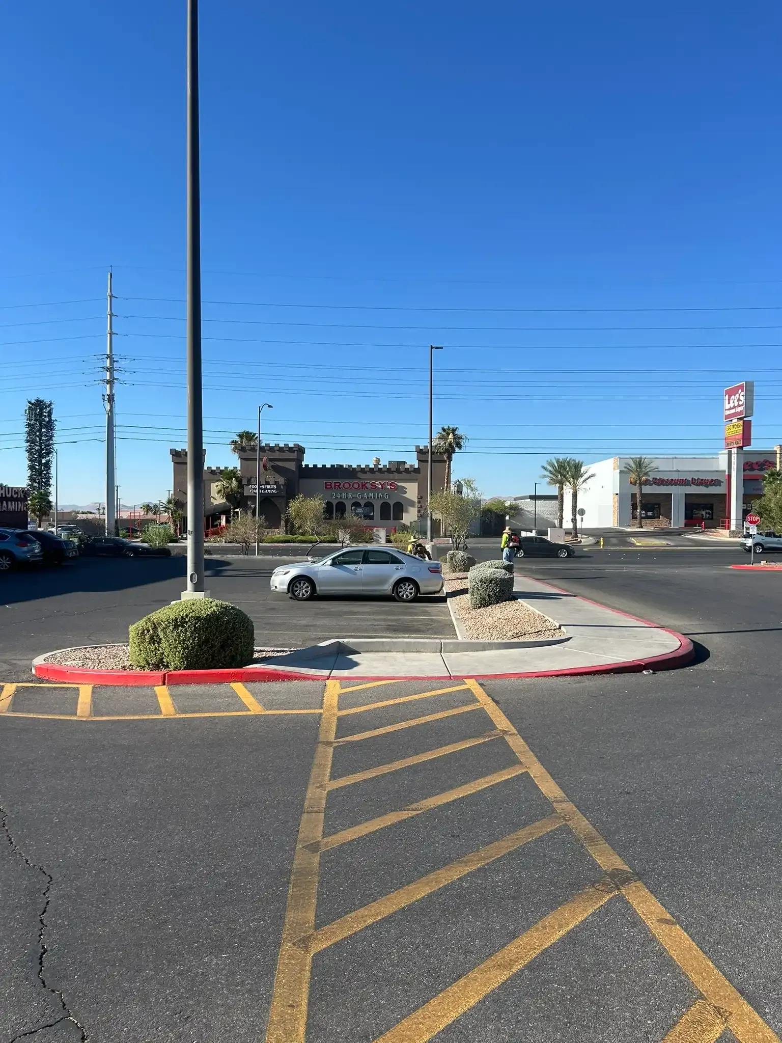 Parking lot with painted crosswalk lines, a silver car, and a traffic signal under a clear blue sky