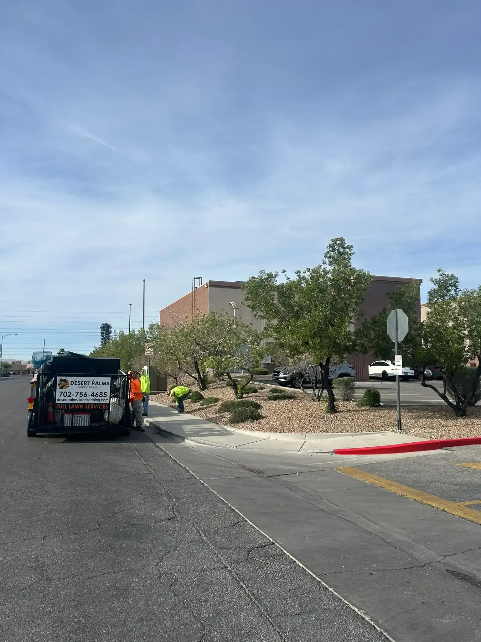 Vehicle and worker near a landscaped curb beside a building on a sunny street.