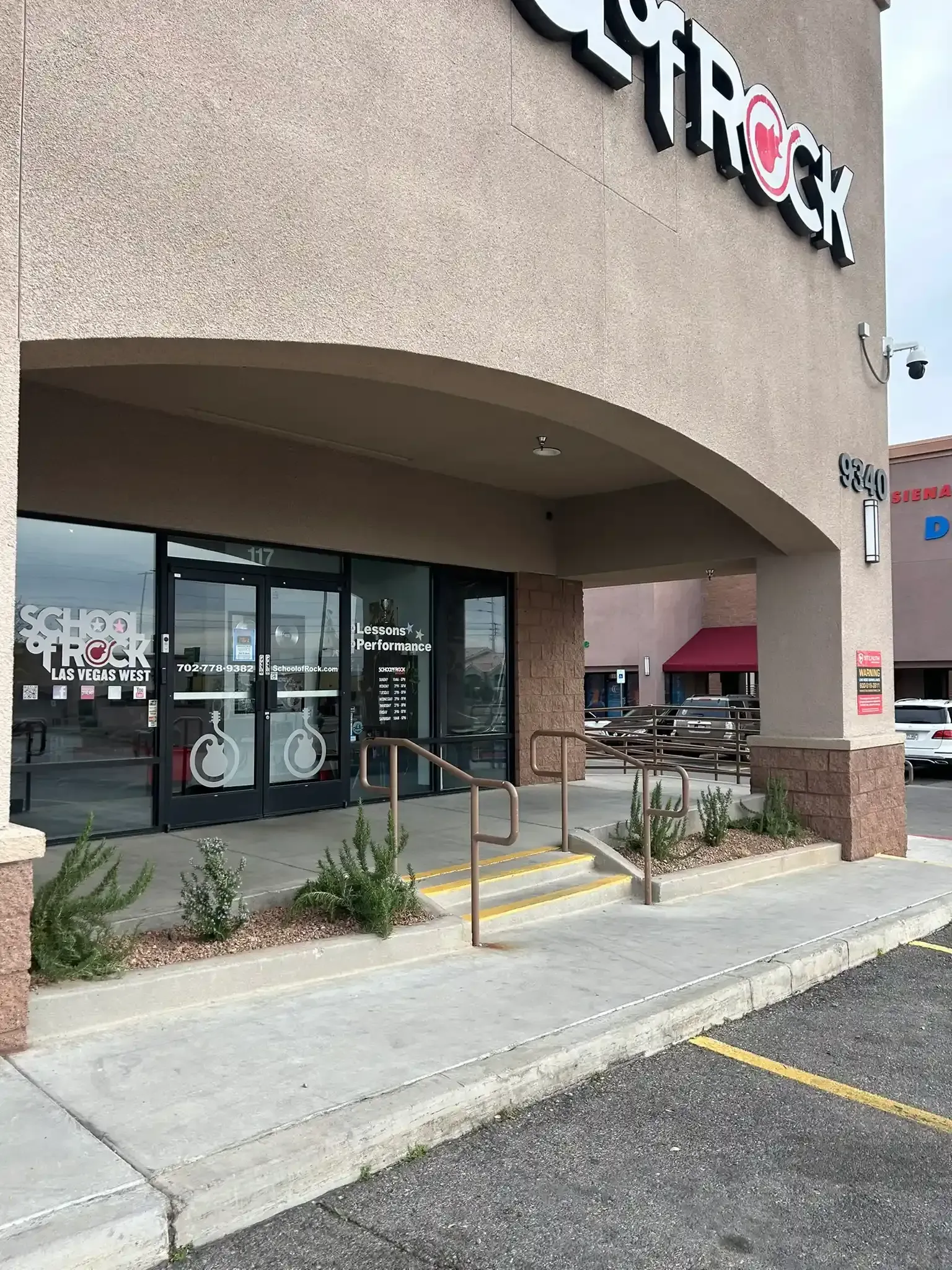 Storefront entrance with glass doors, black awning, and sidewalk ramp in front of a shopping plaza.