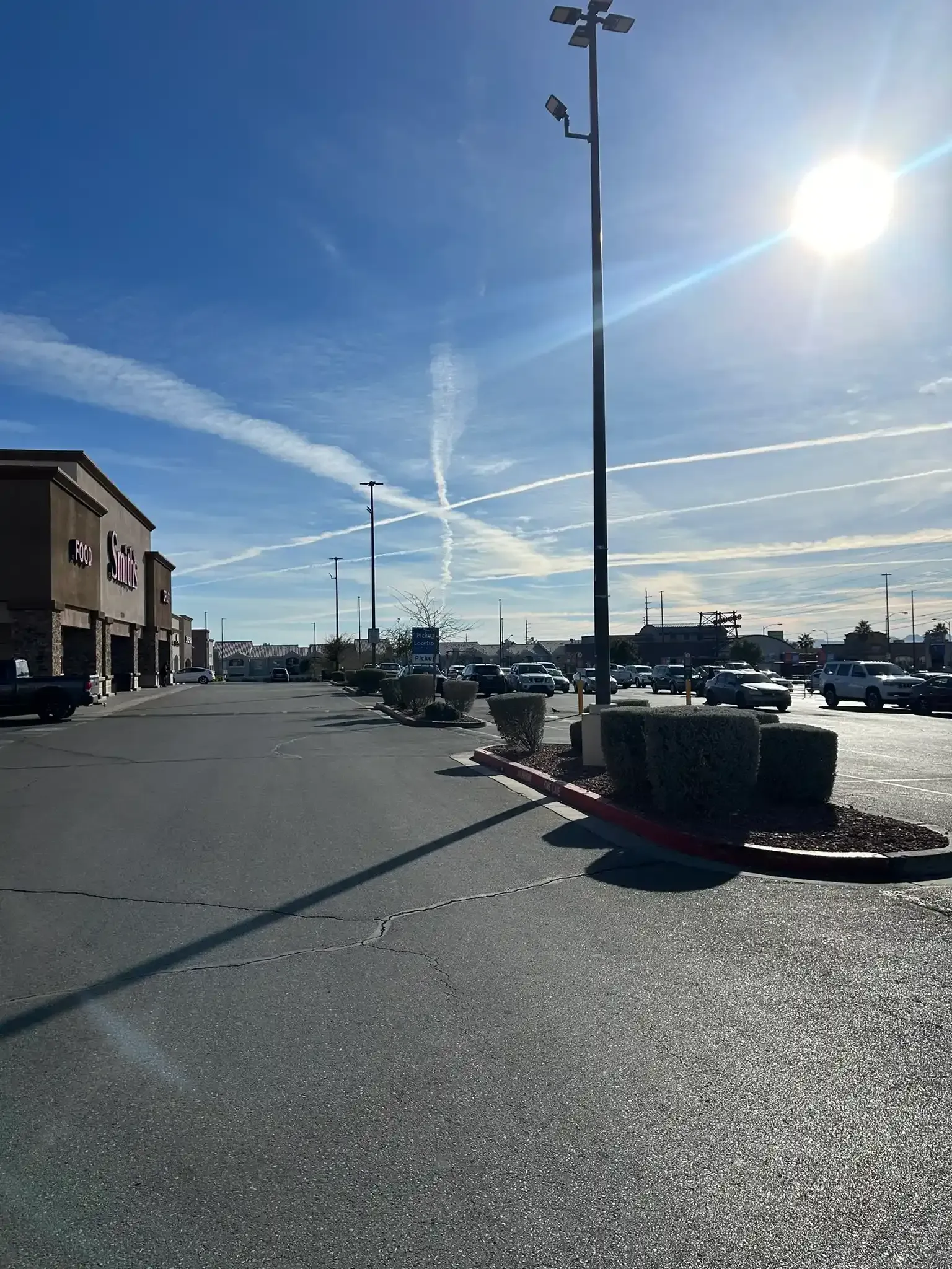 Sunny parking lot beside a building, with cars, a streetlamp, and a bright blue sky with contrails.