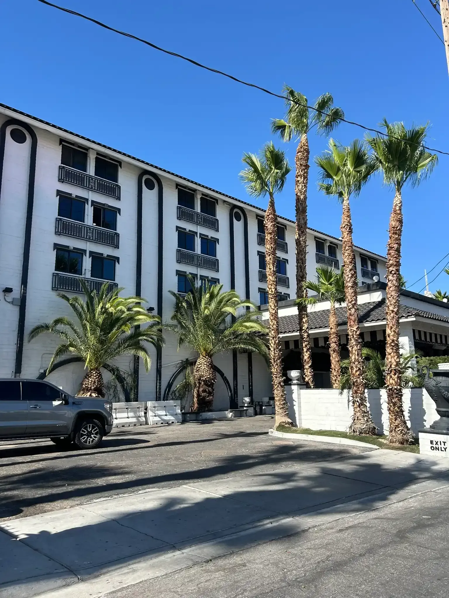White hotel building with palm trees and parked cars under a clear blue sky
