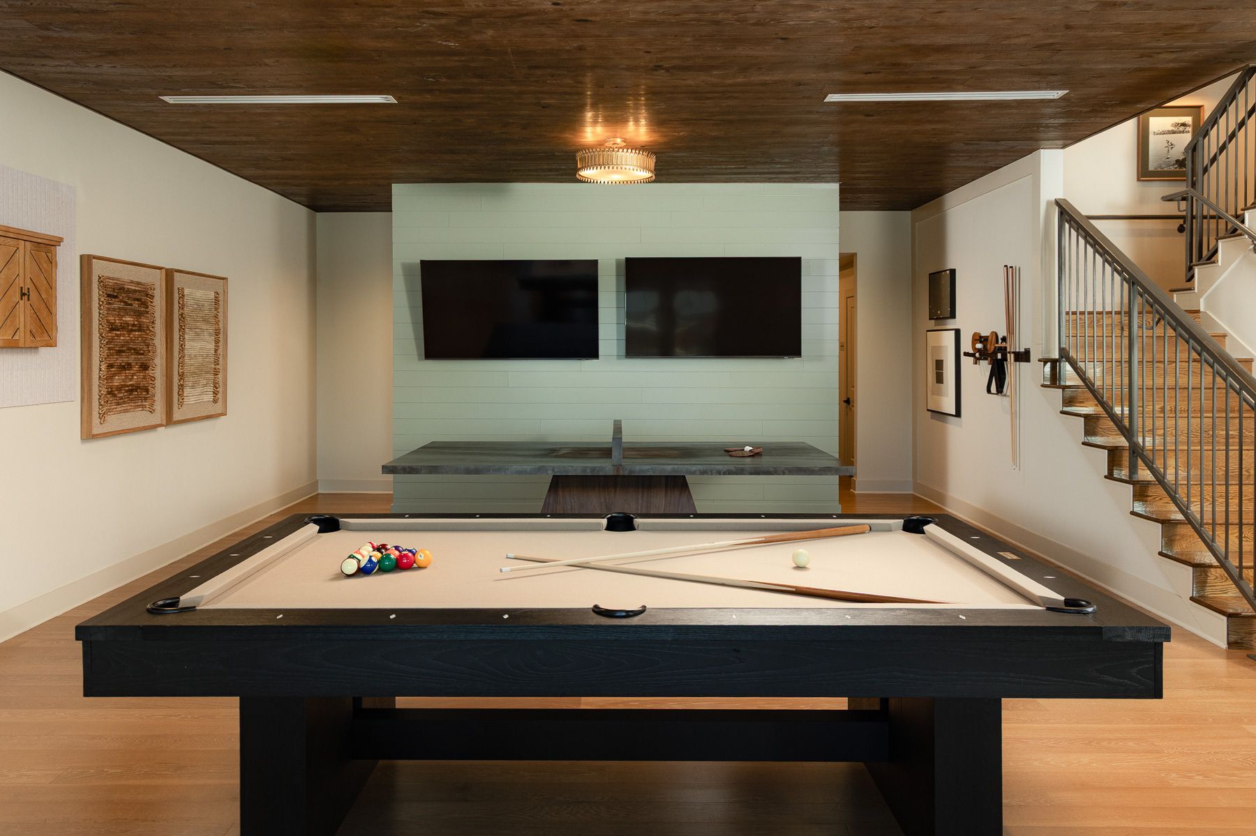 Pool table in a room with a TV, staircase, and art.