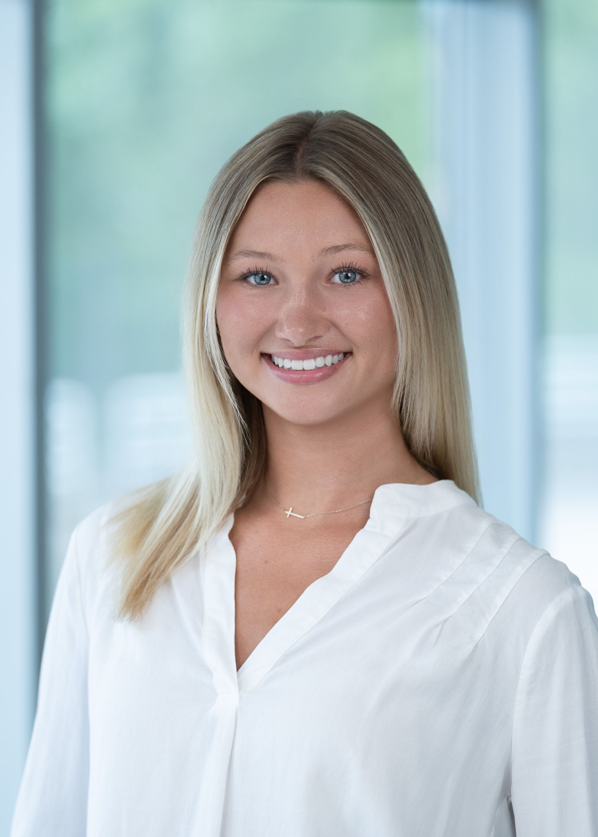 Smiling person in a white blouse standing in front of a bright windowed background