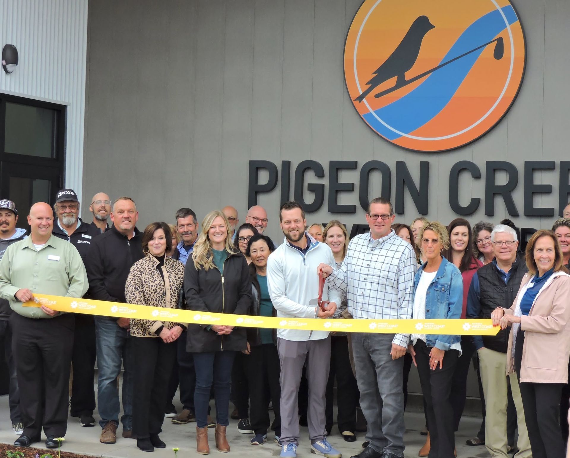 Ribbon-cutting group stands in front of Pigeon Creek sign and logo.