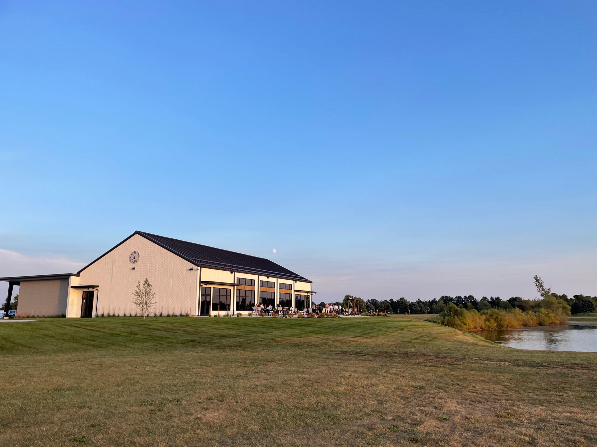 Large white building beside a pond under a clear blue sky, with grassy foreground.