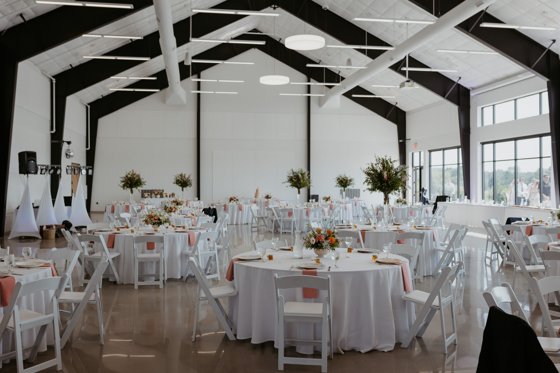 Bright banquet hall with white-draped tables, chairs, and floral centerpieces set for an event