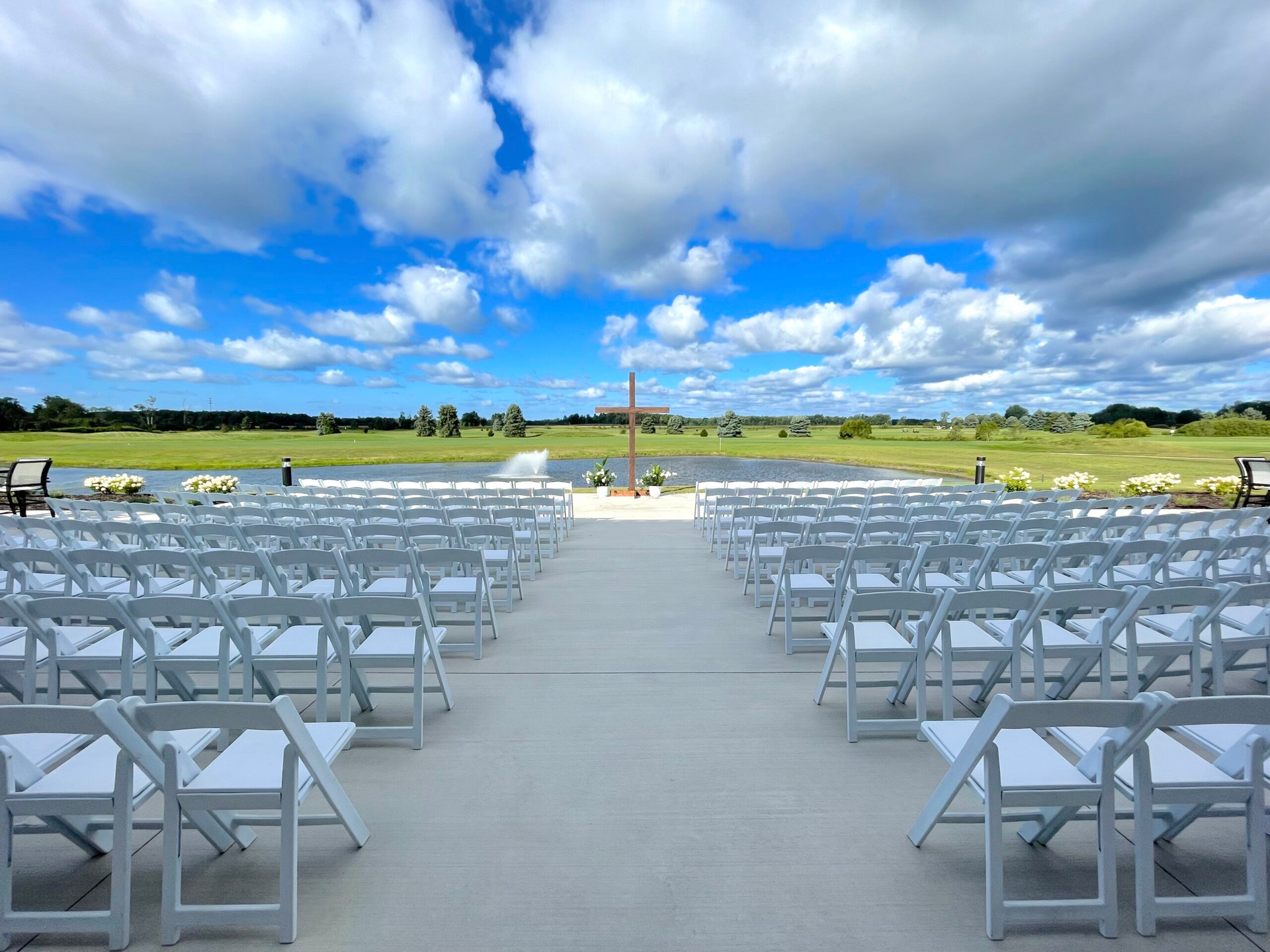 Rows of white chairs set up outdoors on a gray aisle under a bright blue sky with clouds