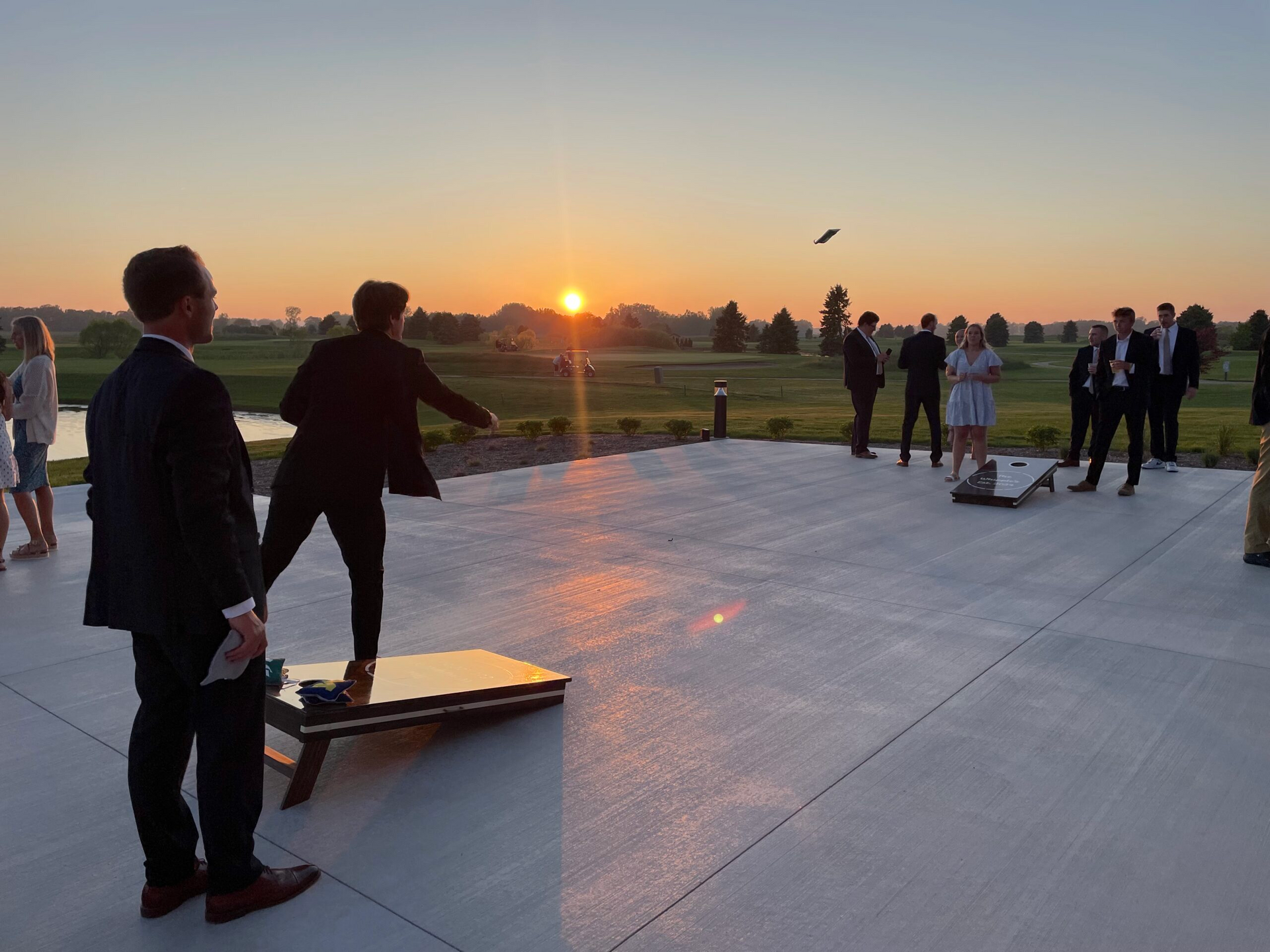 People on a rooftop terrace at sunset, watching a group activity with cornhole boards on the concrete.