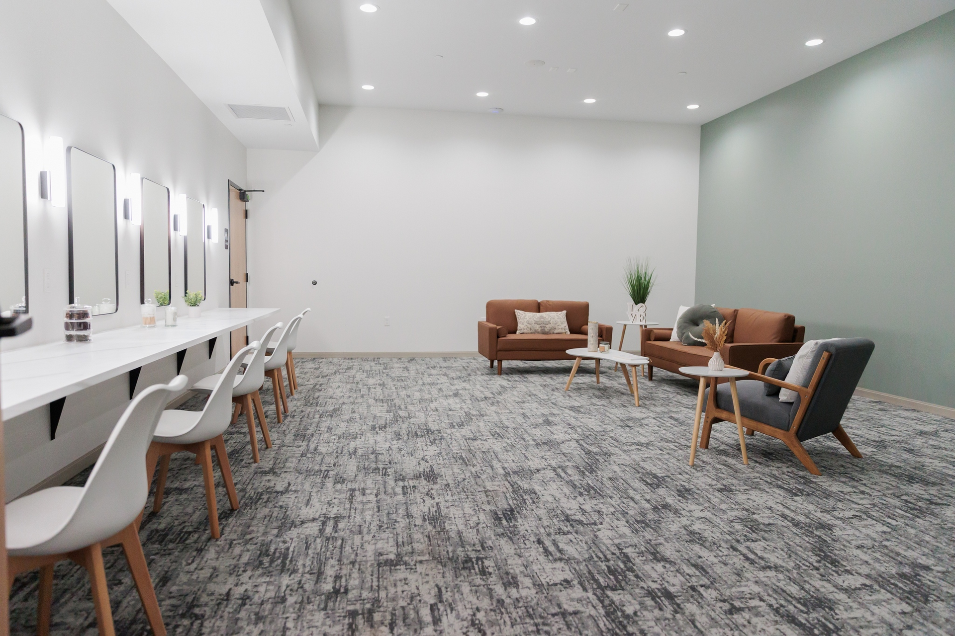 Modern office lounge with white desks, gray carpet, and brown chairs arranged in a spacious room