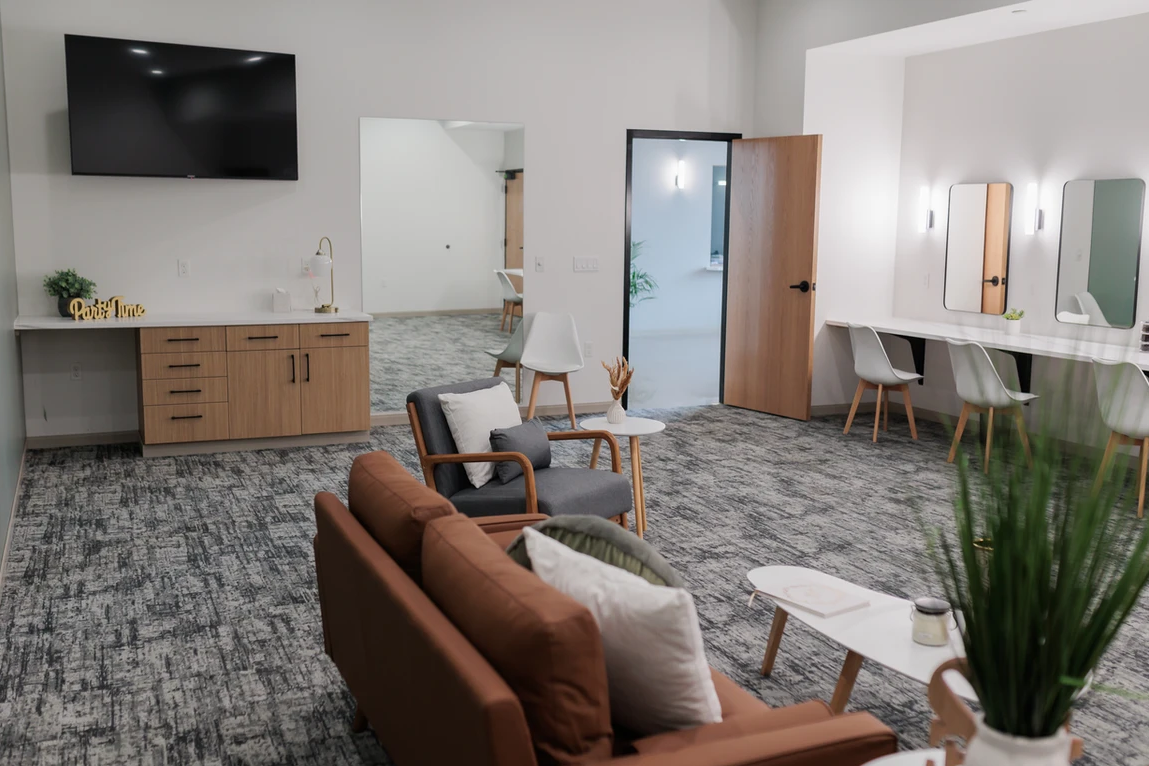 Modern salon waiting area with chairs, mirrors, styling stations, and a wall-mounted TV