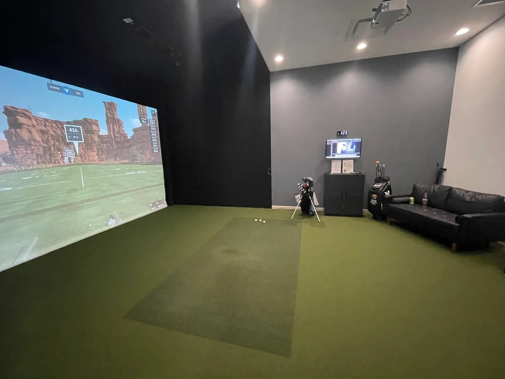Indoor gaming room with green turf, large wall projection, gray walls, and black couch