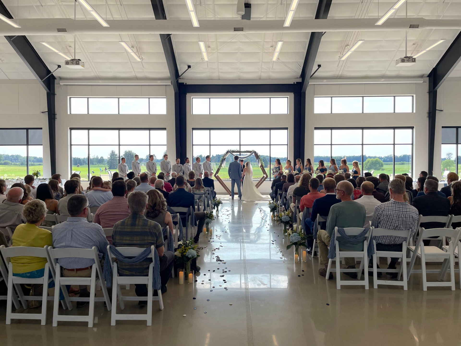 Indoor wedding ceremony with guests seated in rows facing the couple at the front of a bright hall