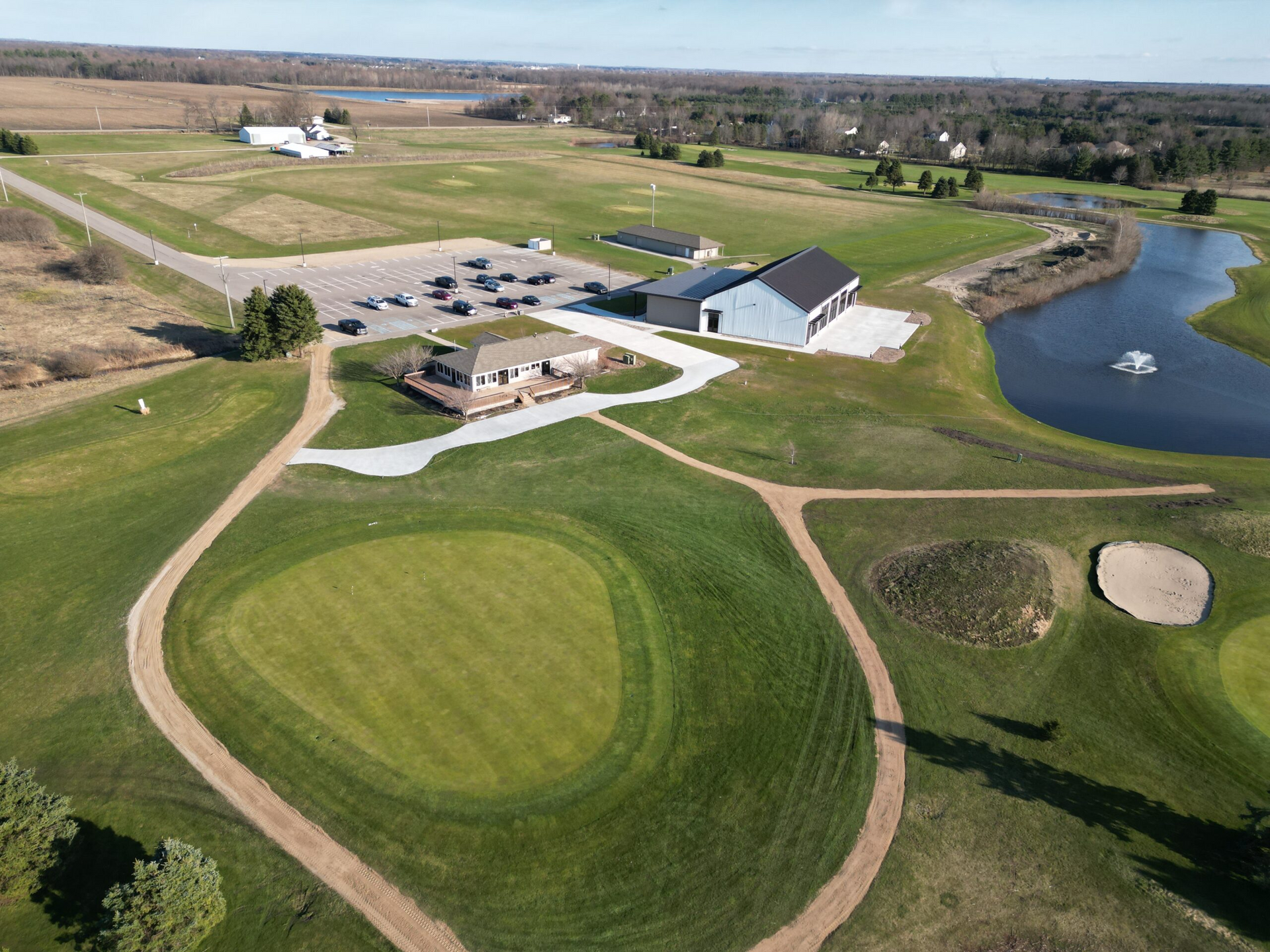 Aerial view of a golf course with green fairways, sand bunkers, clubhouse buildings, and a pond.
