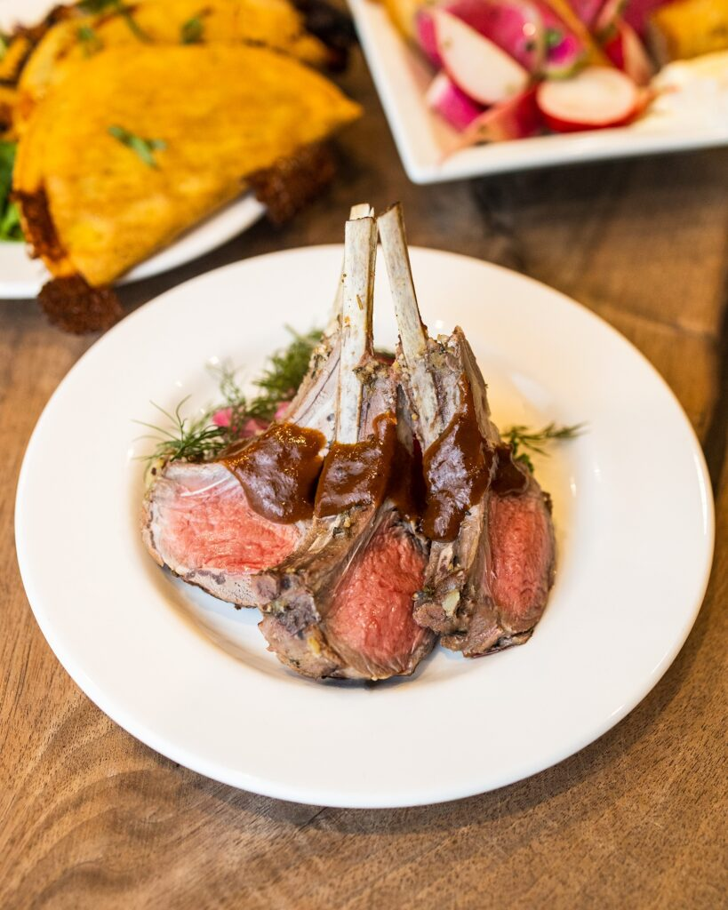 Sliced grilled steak on a white plate with salad and potatoes in the background