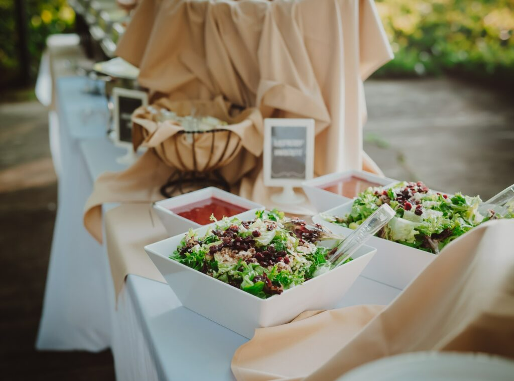 Buffet table with salads in white bowls and beige tablecloths outdoors