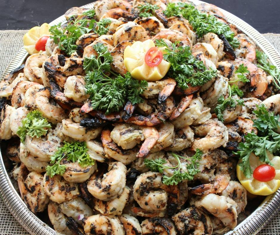Tray of grilled shrimp topped with herbs and lemon slices