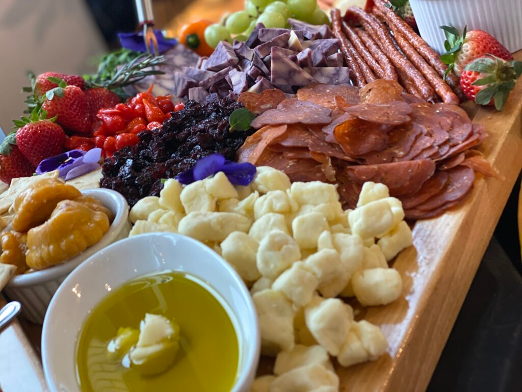Charcuterie board with sliced meats, cheeses, berries, and olive oil dip on a wooden tray