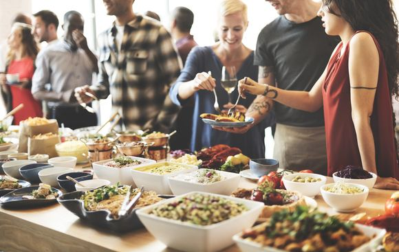 People serving themselves from a buffet table with assorted dishes at a social gathering