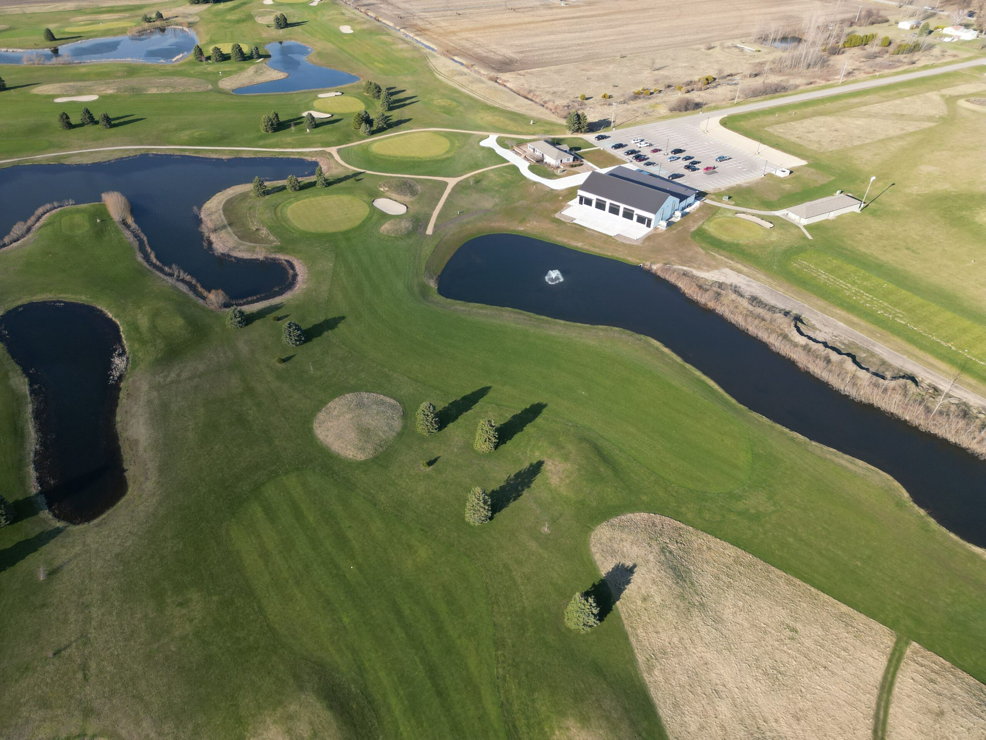 Aerial view of a golf course with fairways, water hazards, and a clubhouse near open fields.