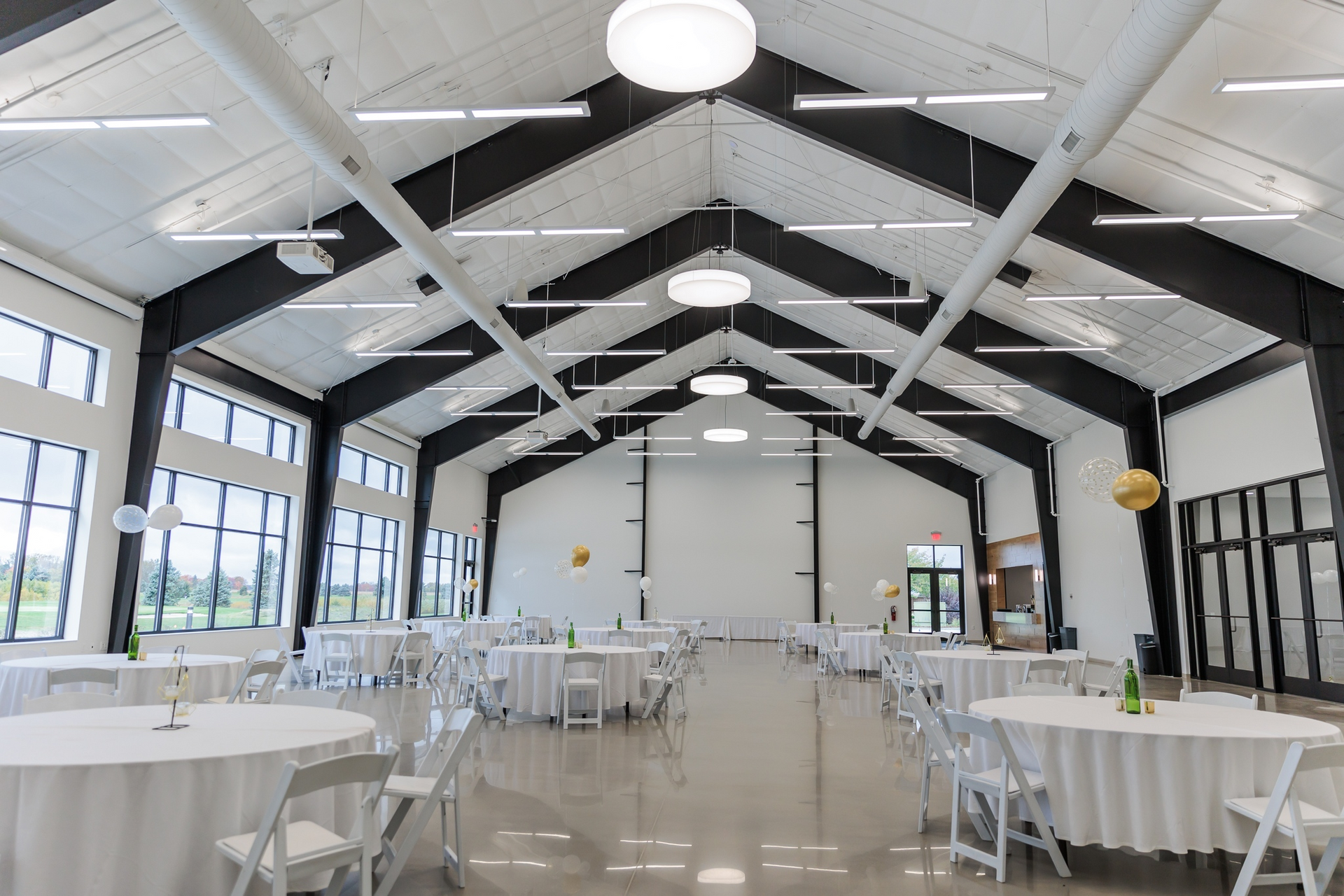 Bright, empty banquet hall with white tables, chairs, and a high black-and-white vaulted ceiling