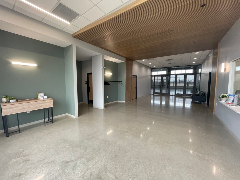 Spacious modern lobby with polished floor, wood-slat ceiling, and glass entry doors.