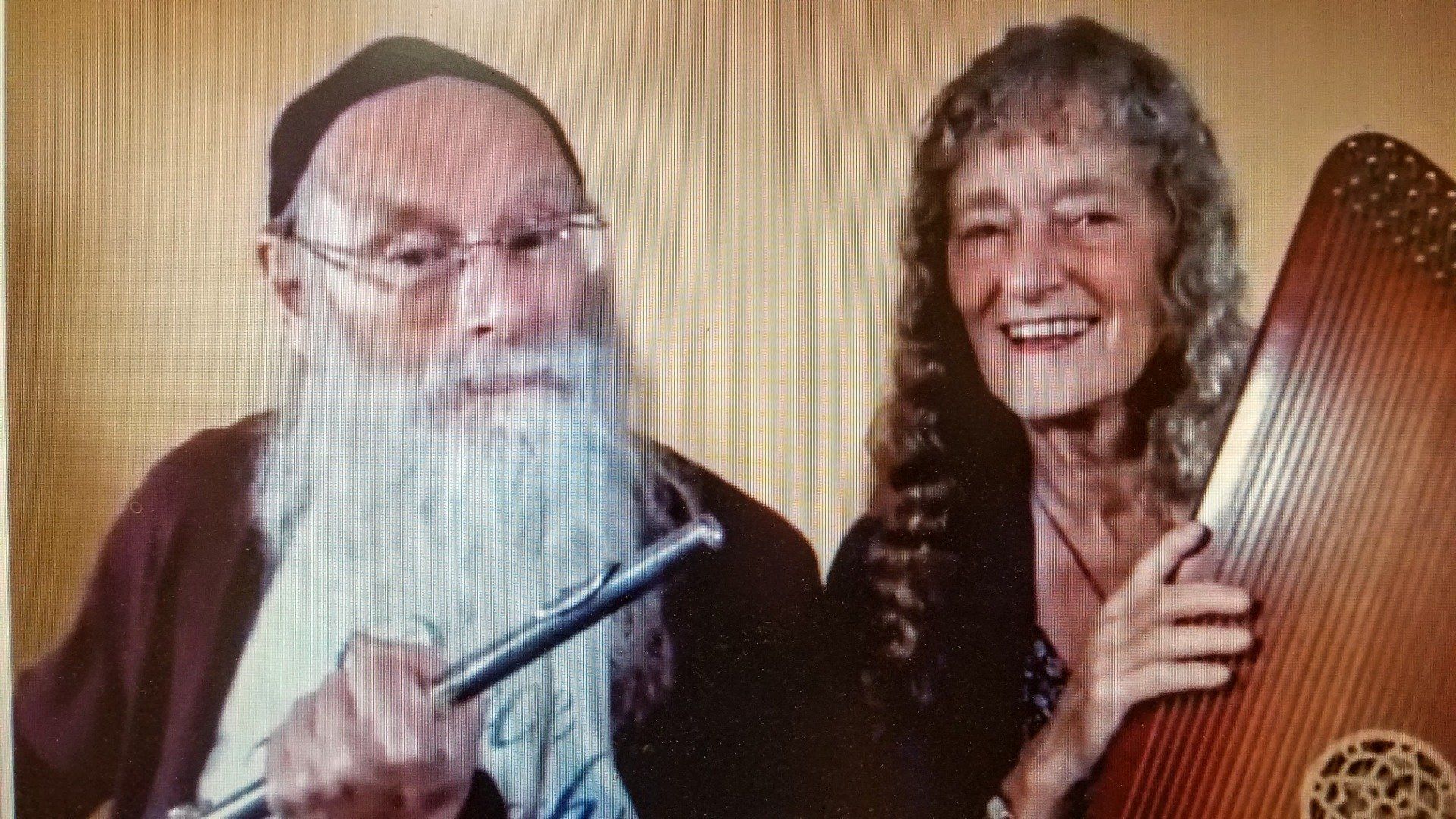 A man with a beard is holding a flute and a woman is holding a harp.