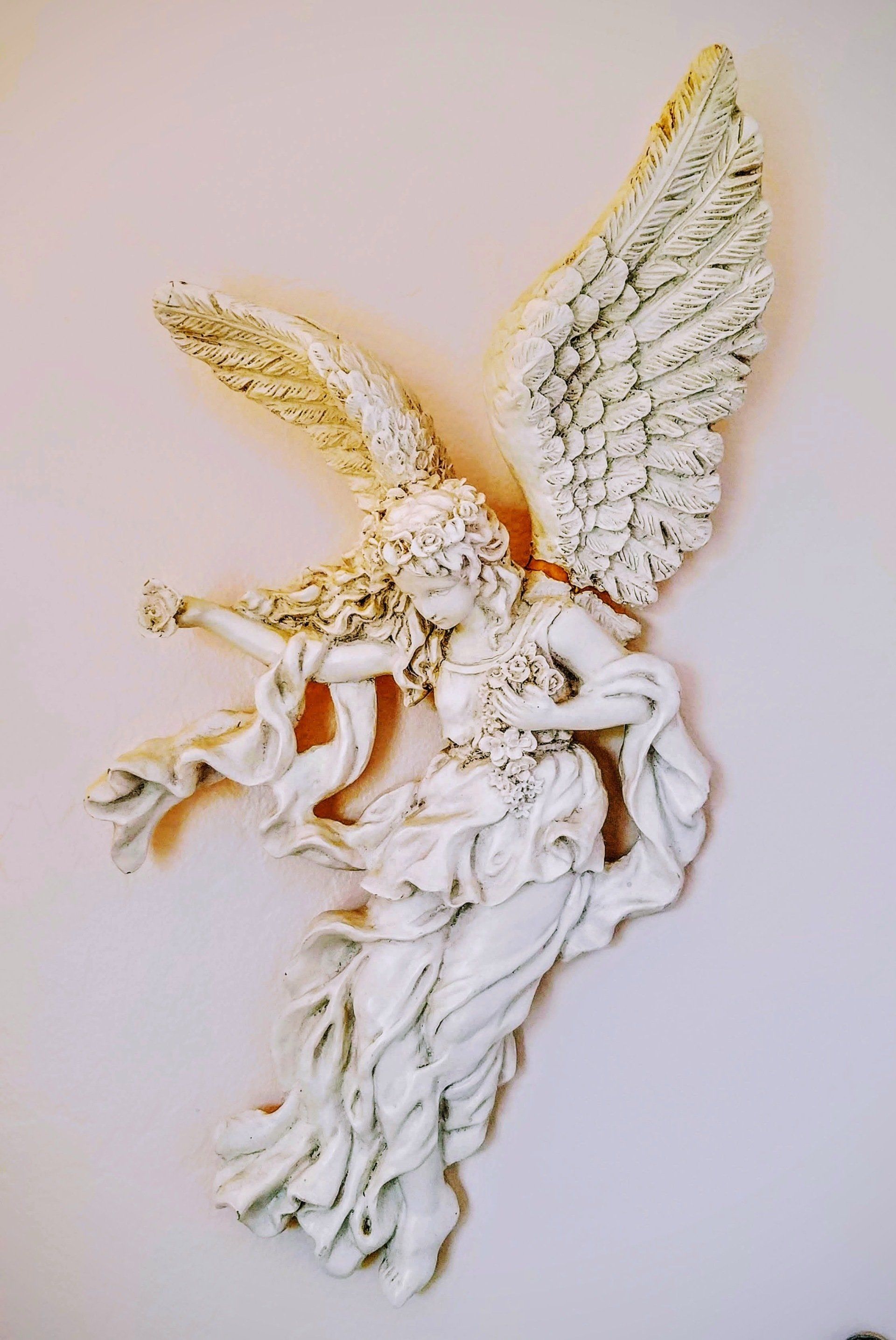 A statue of an angel holding a trumpet on a white wall.