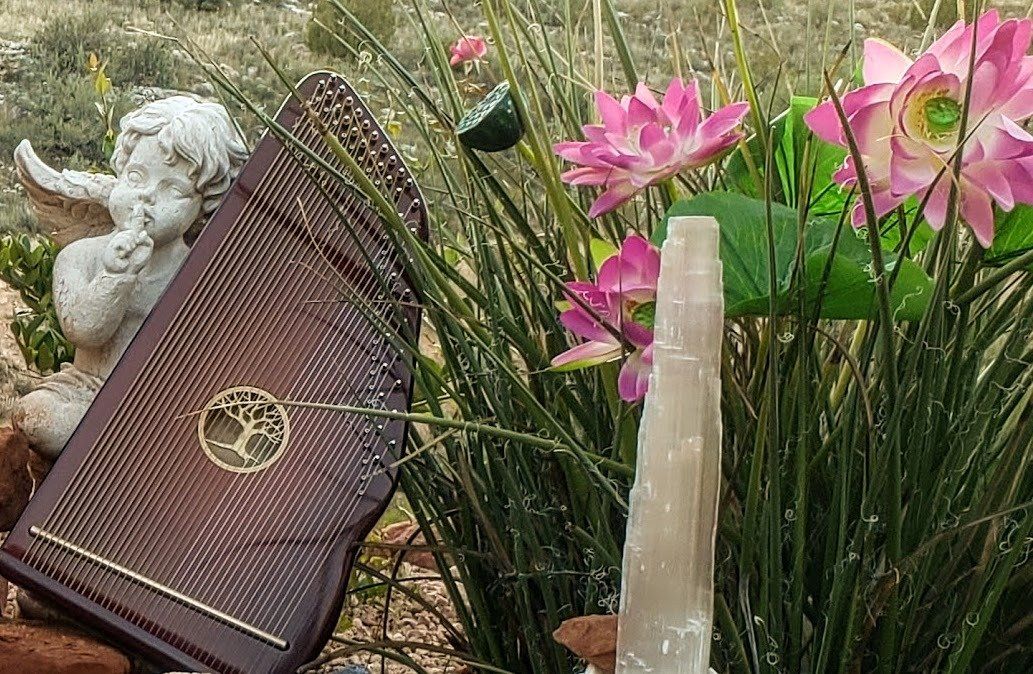 A harp is sitting in a garden next to flowers and a crystal.