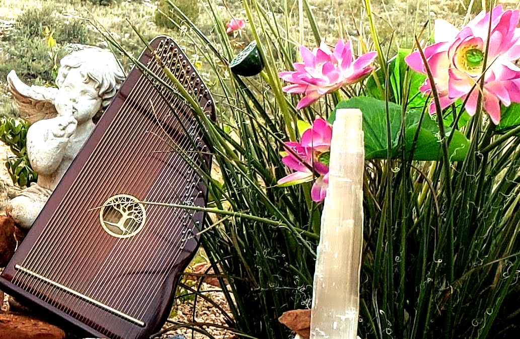 A harp is sitting in a garden next to flowers and a crystal.
