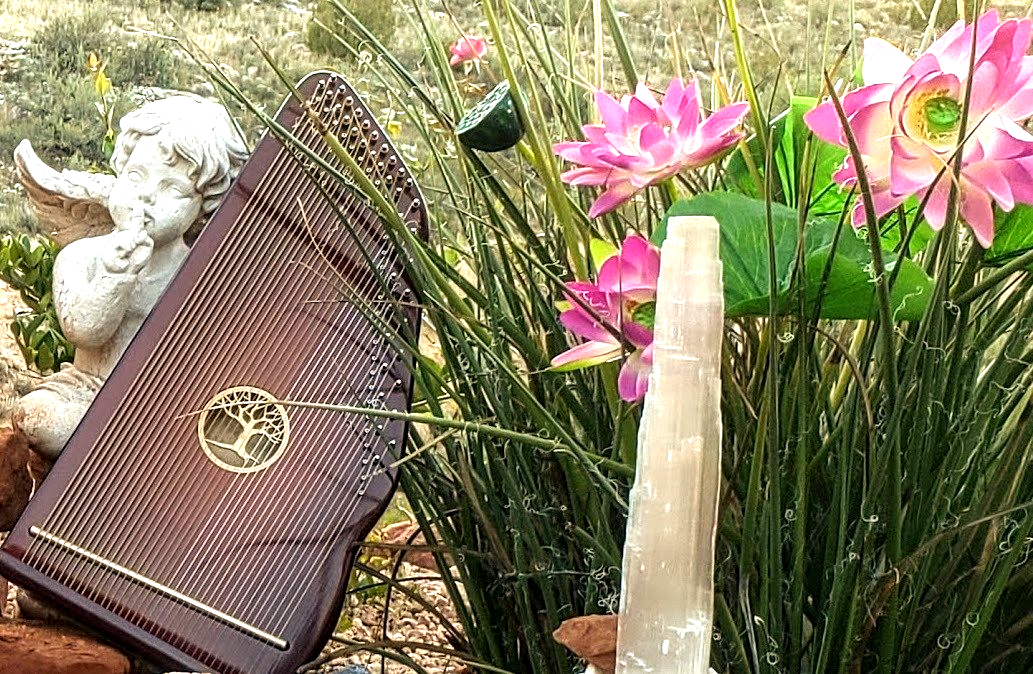 A harp is sitting in a garden next to flowers and a crystal.