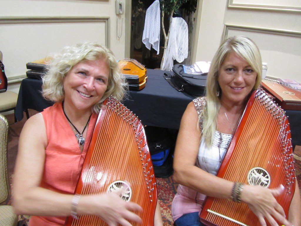 Two women are playing harps and smiling for the camera