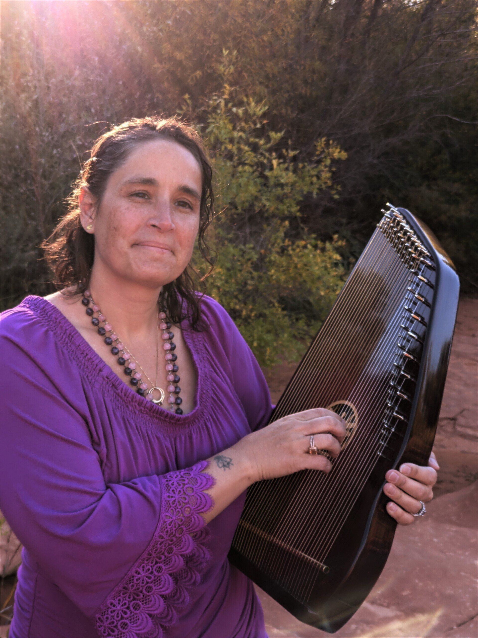A woman in a purple shirt is holding a harp.