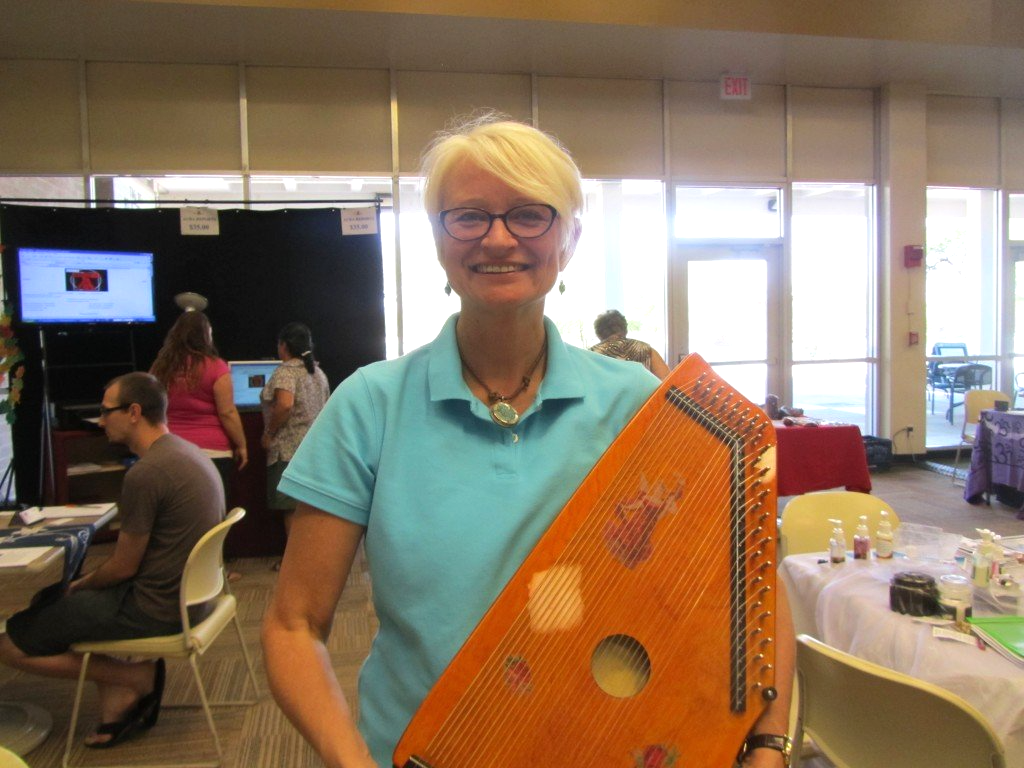 A woman in a blue shirt is holding a harp and smiling.