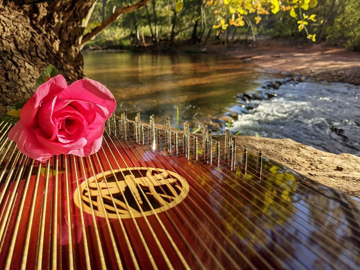 A pink rose sits on top of a harp with a river in the background