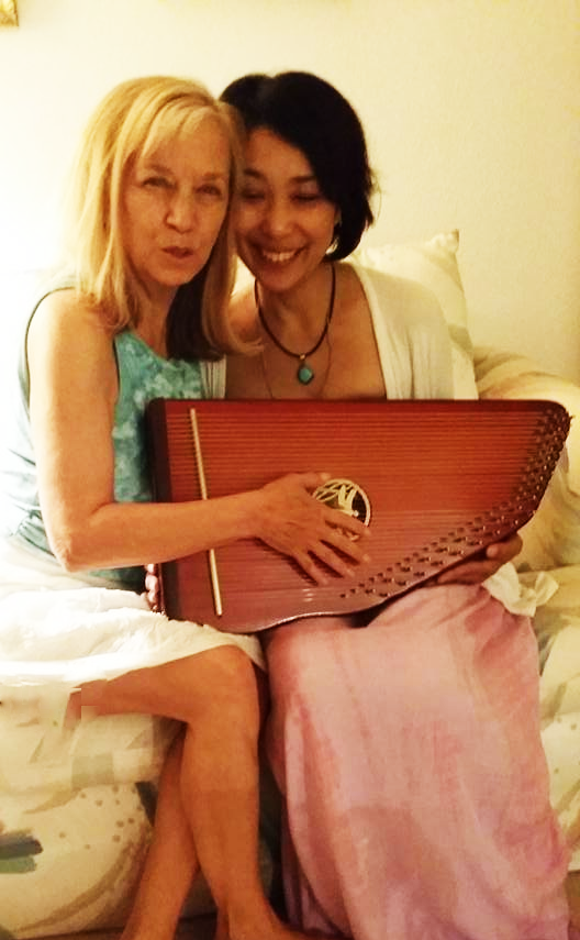 Two women are sitting next to each other holding a harp.