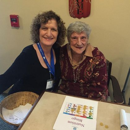 Two women sitting at a table with a book titled nutrition bingo.