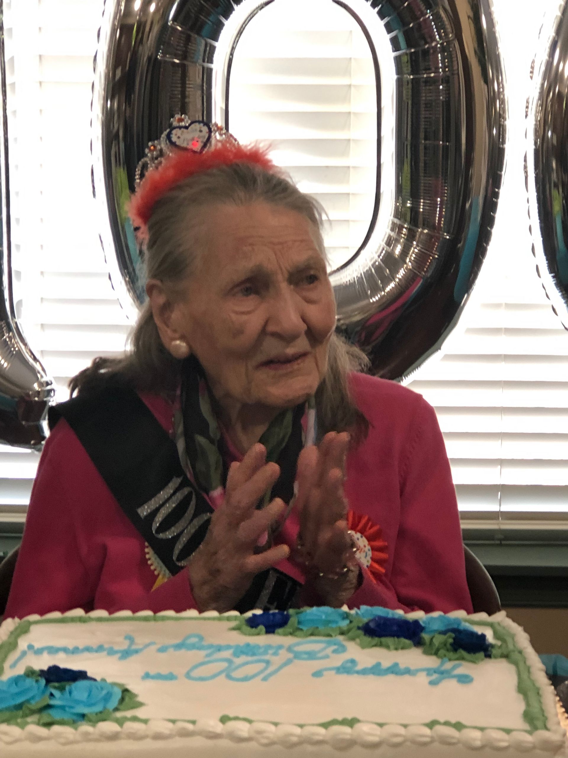 An elderly woman wearing a sash with the number 100 on it