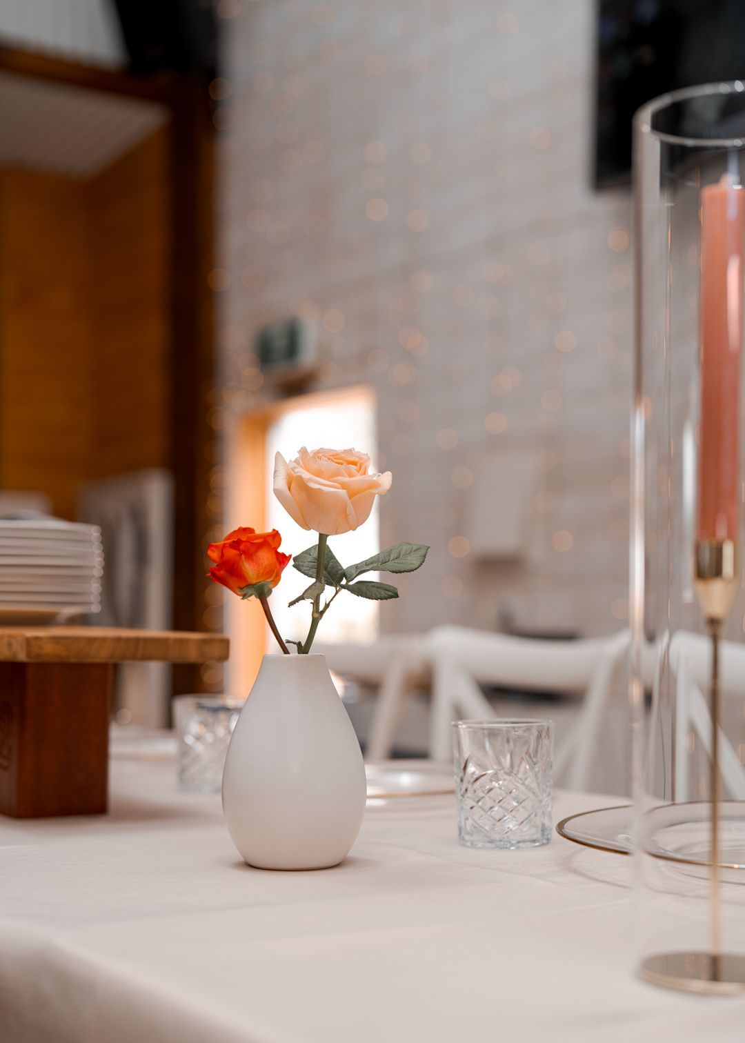 Small white vase with orange and white flowers on a table in a softly lit room