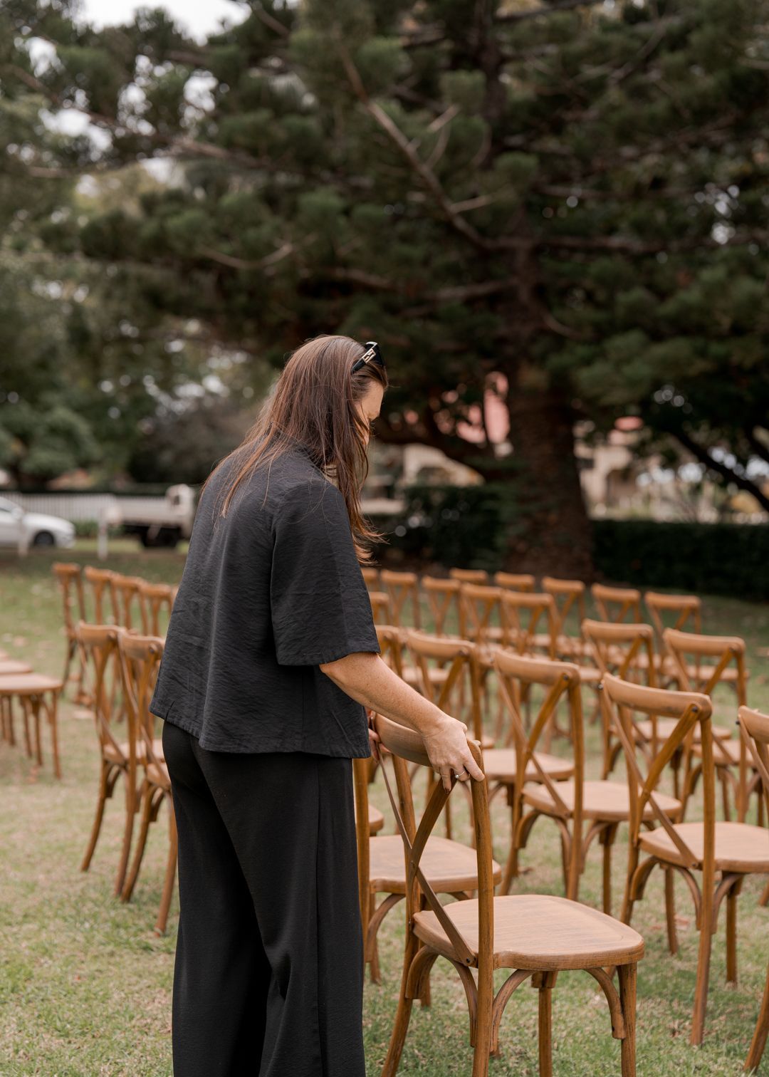 Person arranging wooden chairs on a grassy lawn outdoors.