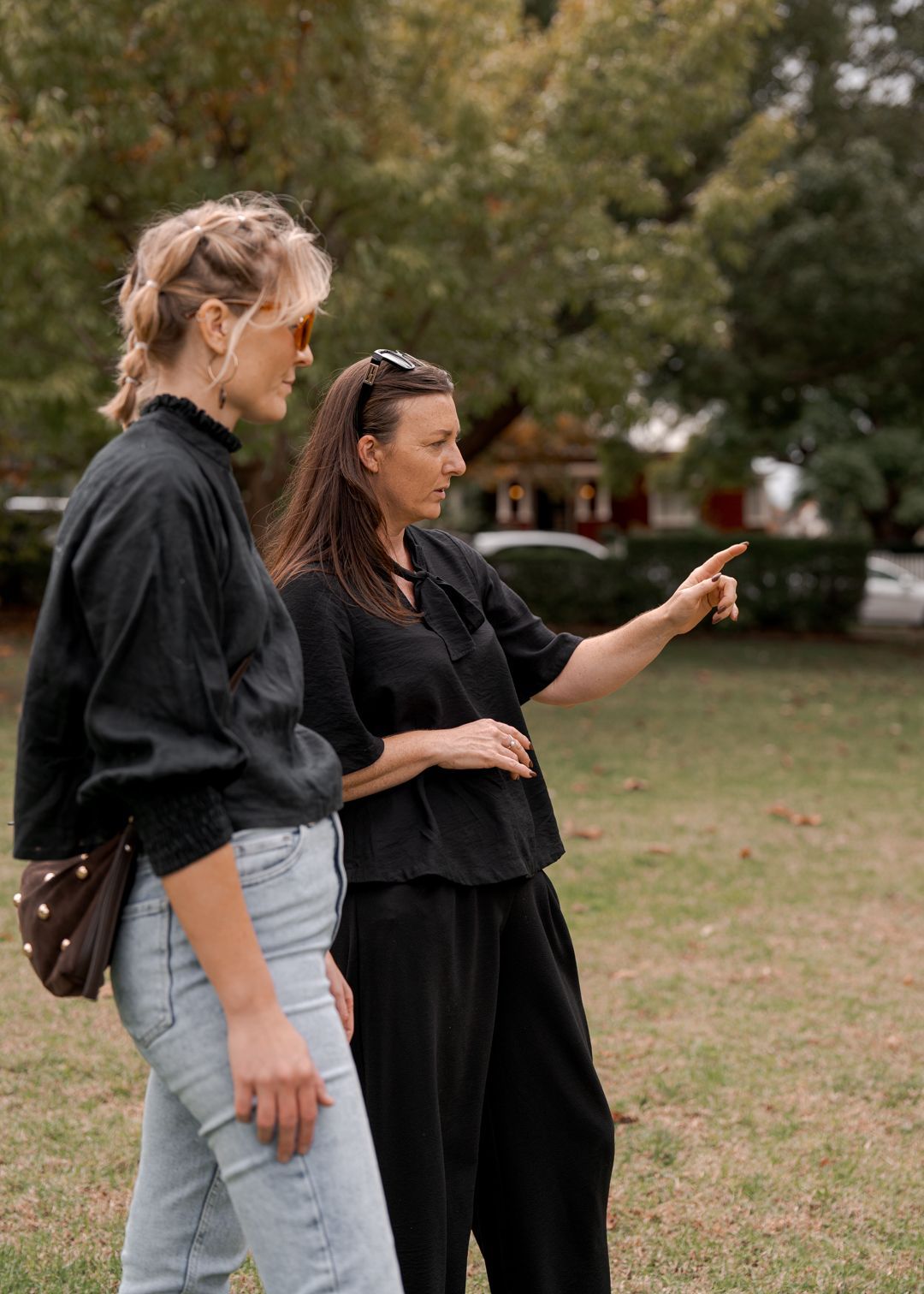 Two people in dark clothing standing outdoors, one pointing across a grassy park.